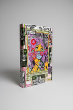 A square mixed-media collage art trading card box. Featuring a stylized illustration of a woman with purple hair and a face mask, surrounded by graffiti, text, and graphic elements, displayed on a wooden surface.