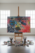 A large colorful canvas painting on an easel in a bright studio, showing a comic-style battle scene. Paintbrushes and paint containers are scattered on the floor around the easel.